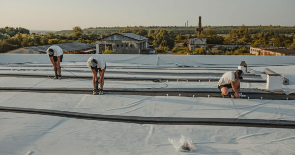 Construction worker drill with a powerful electric drill synthetic membrane for a new roof.